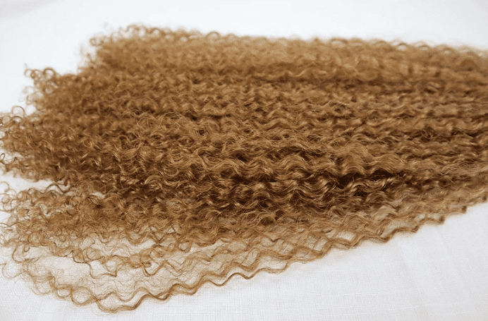 Curly light brown hair weft on a white background.