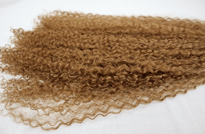 Curly light brown hair weft on a white background.